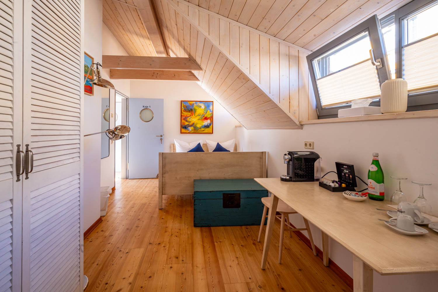 [Doppelzimmer »Koje 1« 402] Helles Doppelzimmer im Neuen Fährgut mit gemütlichem Doppelbett, Blick auf die Dorfstraße zur Elbe und Zugang zur gemeinsamen Terrasse mit Zimmer 403.